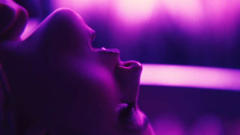 Filmstill zu TOUCH ME. Profilansicht eines Gesichts mit geöffnetem Mund in violettem Licht.